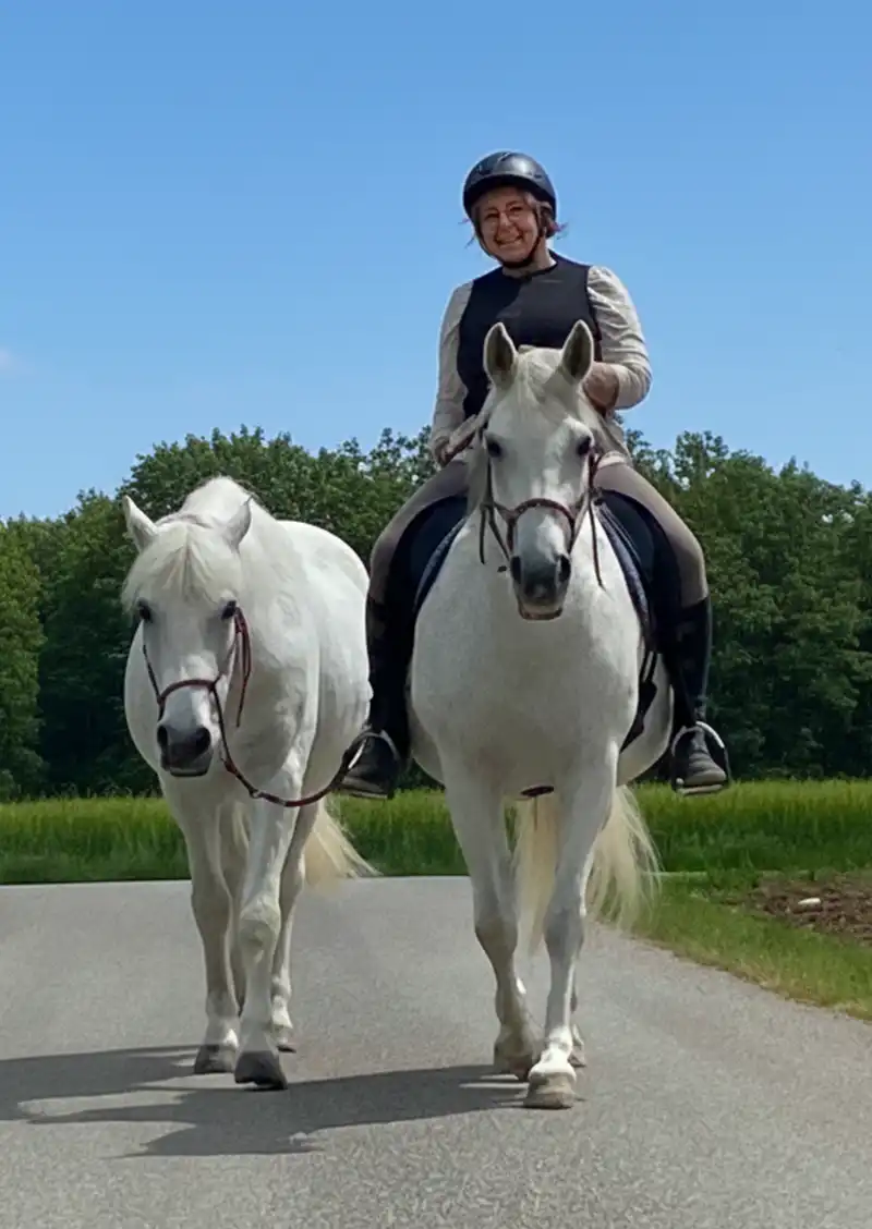 Eine Frau reitet auf einem Schimmel und führt ein Pferd mit sich